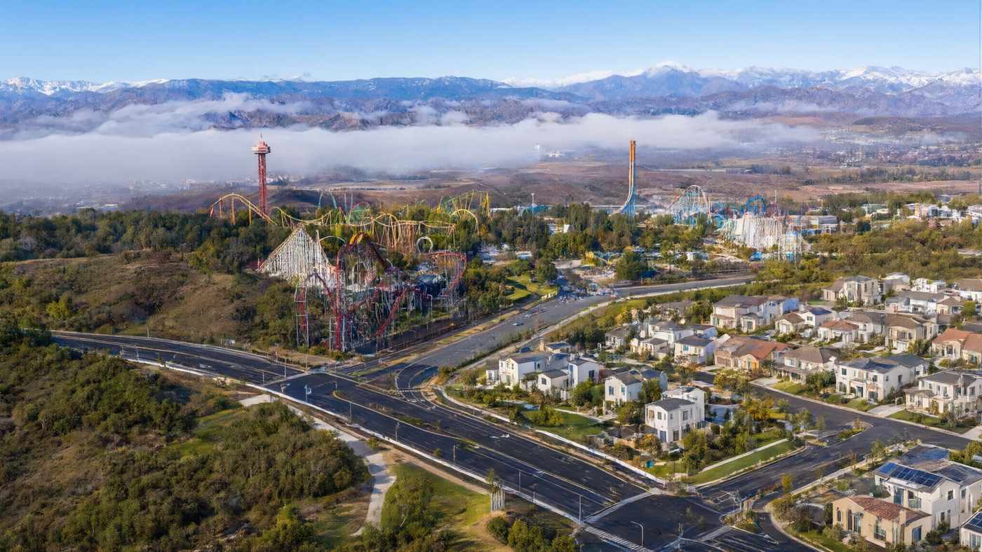 Aerial view over Santa Clarita Valley hills and rooftops toward a theme park's roller coasters (illustrative image)