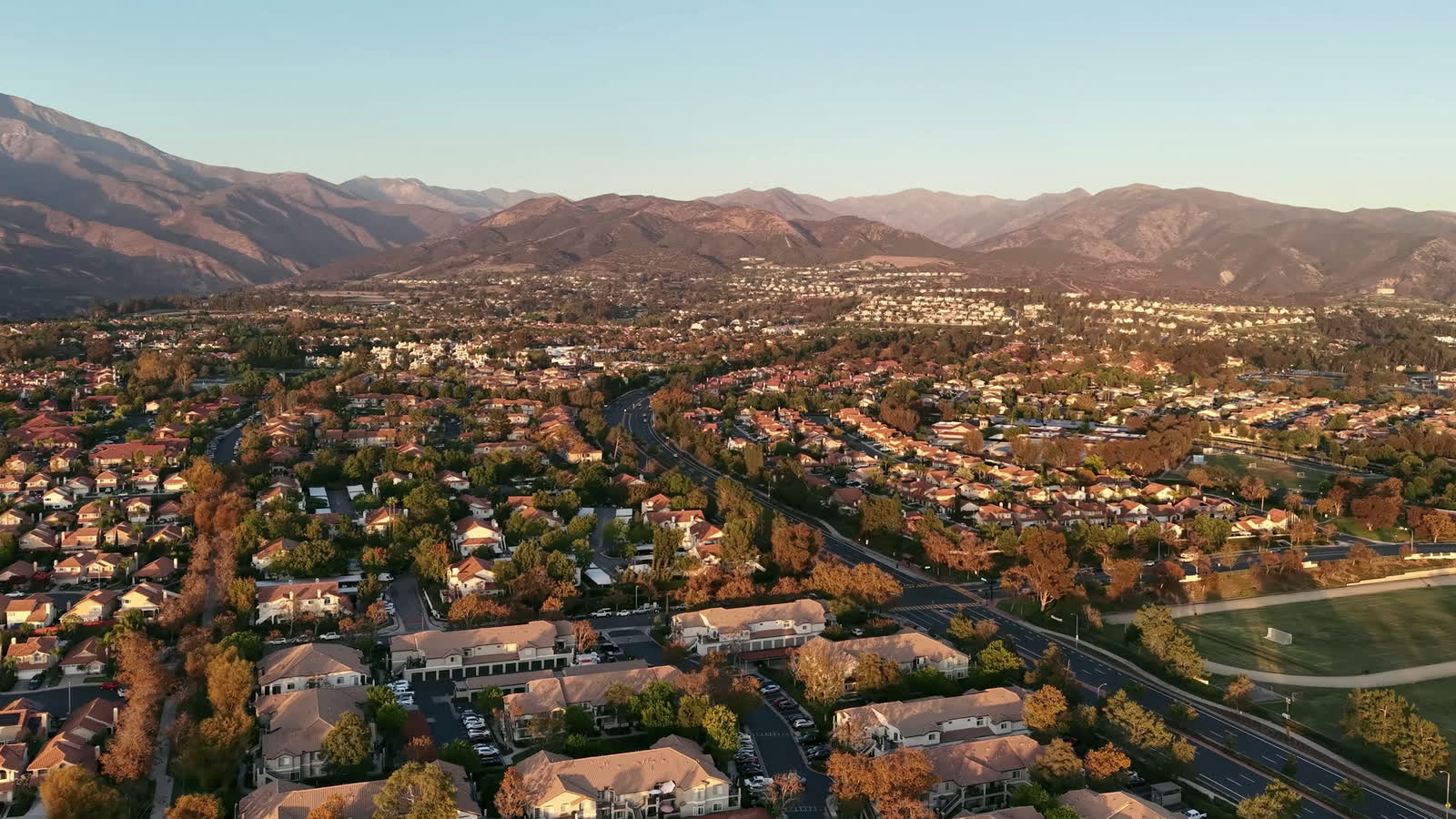 Drone view at golden hour over a Southern California neighborhood with mountains behind (illustrative stock footage)